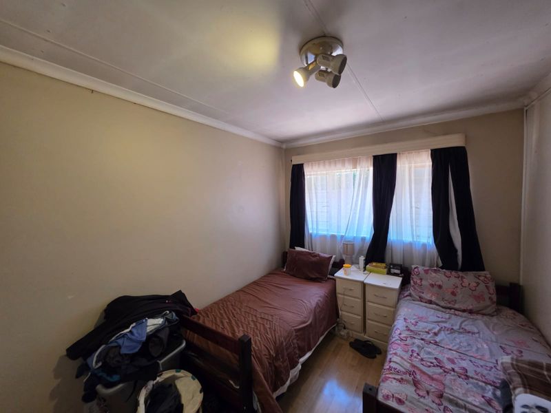 A compact bedroom featuring laminate flooring, a ceiling-mounted spotlight fixture, and a window fitted with security bars.