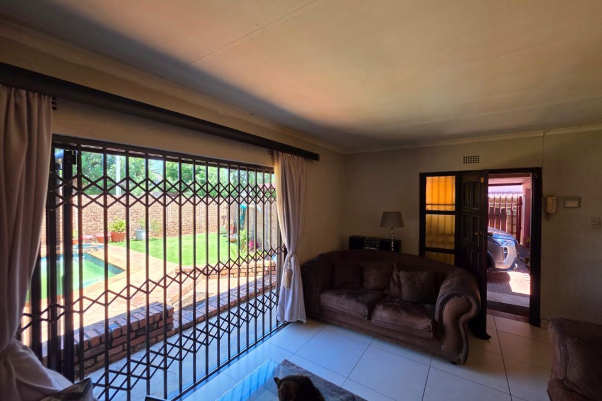 A living room featuring tiled flooring and a large sliding door with a security gate, providing direct access to the outdoor pool area.