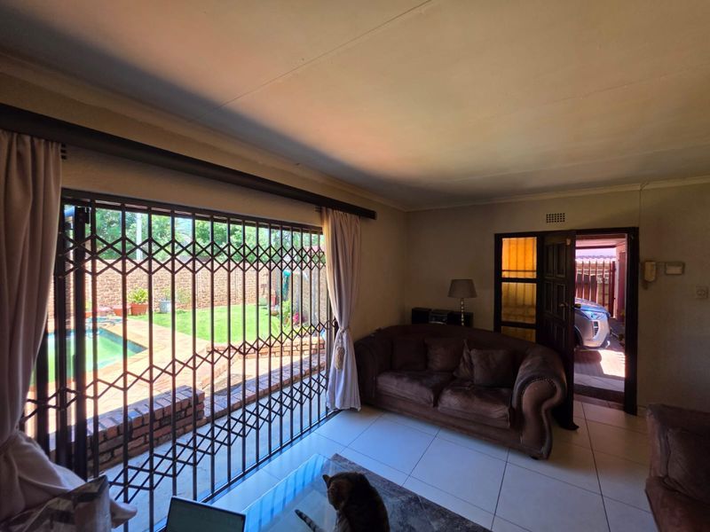A living room featuring tiled flooring and a large sliding door with a security gate, providing direct access to the outdoor pool area.