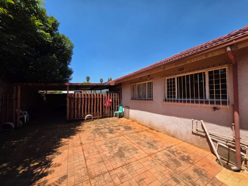 Rear exterior view featuring a paved patio area, covered carport, and security-barred windows on a single-story residential structure.