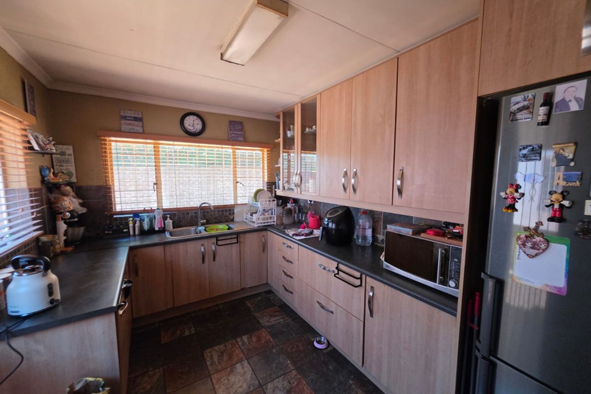 A functional kitchen featuring wood-look laminate cabinetry, dark countertops, slate flooring, and a tiled backsplash, offering a practical layout for daily use.