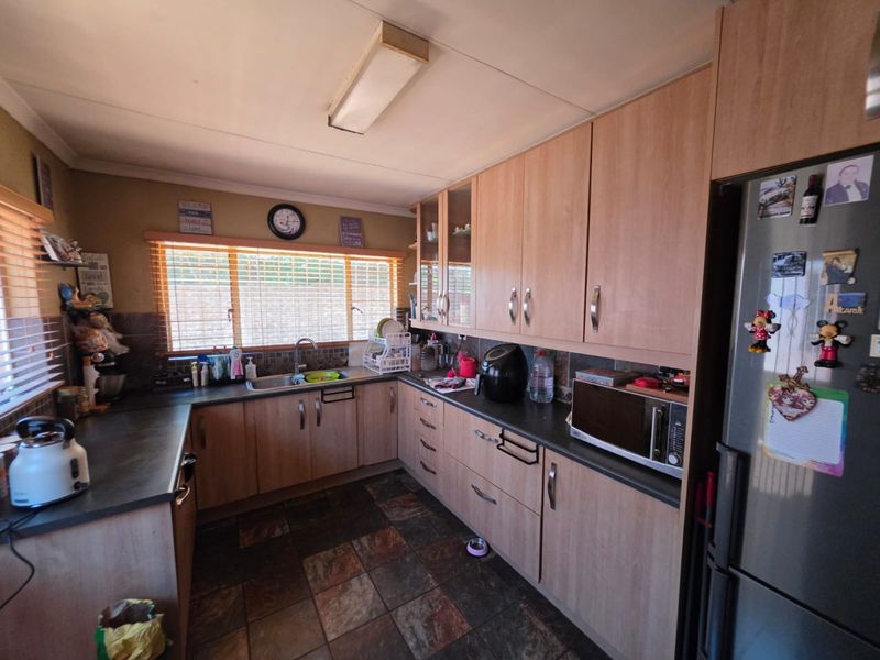 A functional kitchen featuring wood-look laminate cabinetry, dark countertops, slate flooring, and a tiled backsplash, offering a practical layout for daily use.