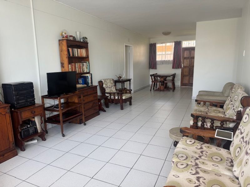 An open-plan living and dining area featuring white walls and tiled flooring, providing a functional and versatile space for daily living.
