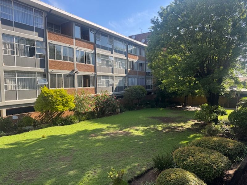 View of the apartment building's rear facade featuring brick construction and large windows overlooking a well-maintained communal garden area.