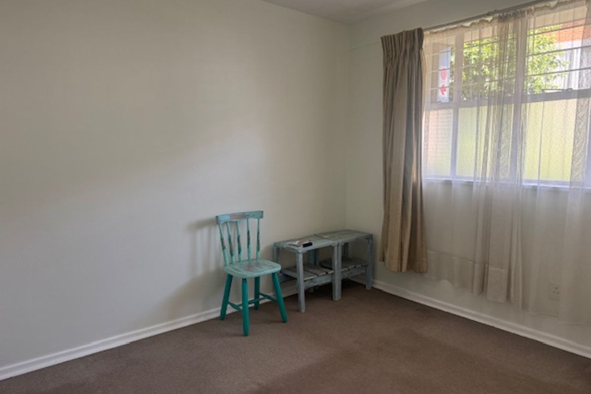 A simple, carpeted bedroom featuring a window with security bars and neutral wall finishes, offering a blank canvas for personalization.