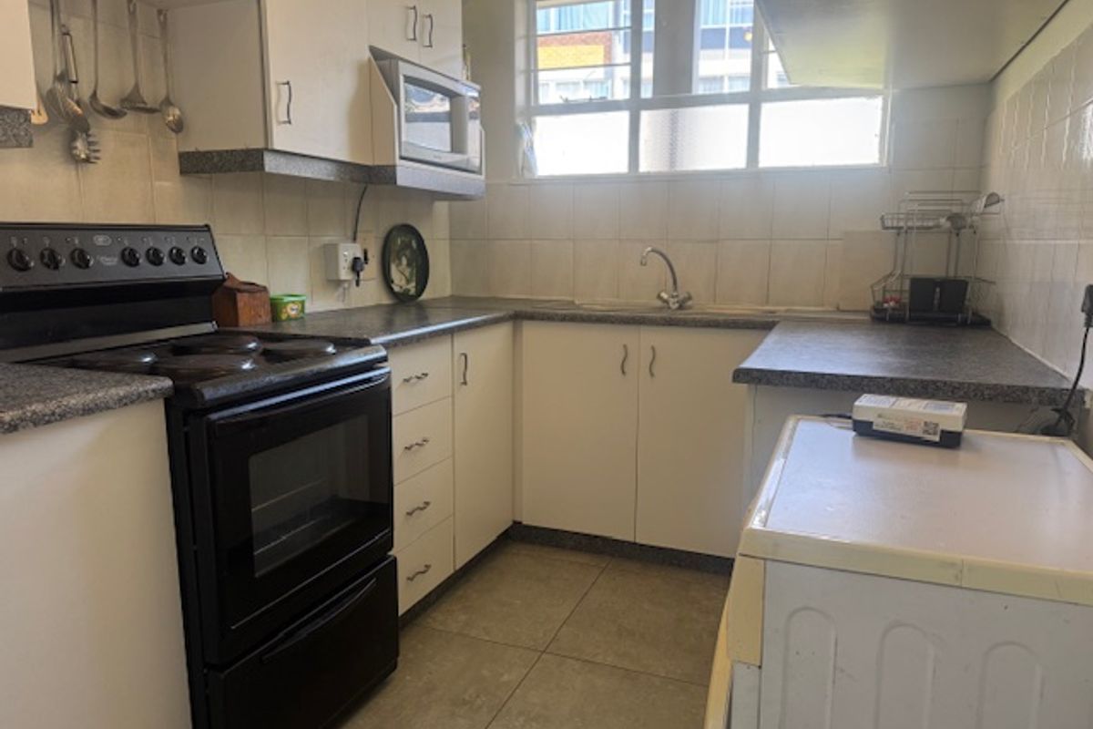 Functional kitchen featuring laminate countertops, tiled splashbacks, built-in cabinetry, and a stainless steel sink, offering a practical layout with potential for modern updates.