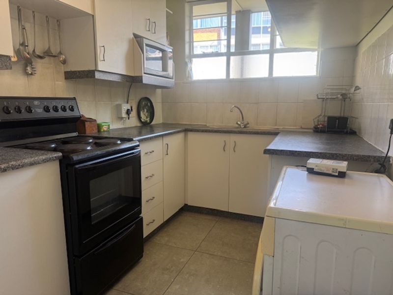 Functional kitchen featuring laminate countertops, tiled splashbacks, built-in cabinetry, and a stainless steel sink, offering a practical layout with potential for modern updates.
