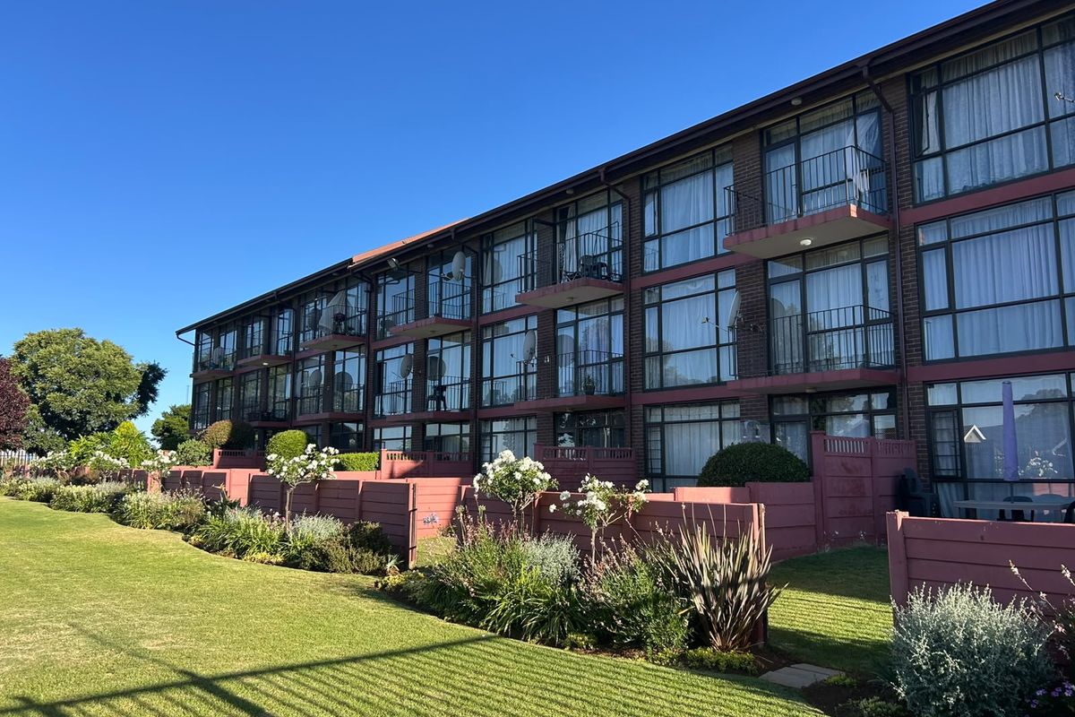 A view of the rear elevation of a multi-story apartment building featuring brick construction, private balconies, and well-maintained landscaped garden areas.