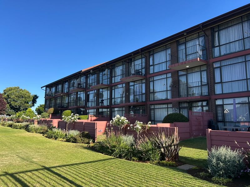 A view of the rear elevation of a multi-story apartment building featuring brick construction, private balconies, and well-maintained landscaped garden areas.