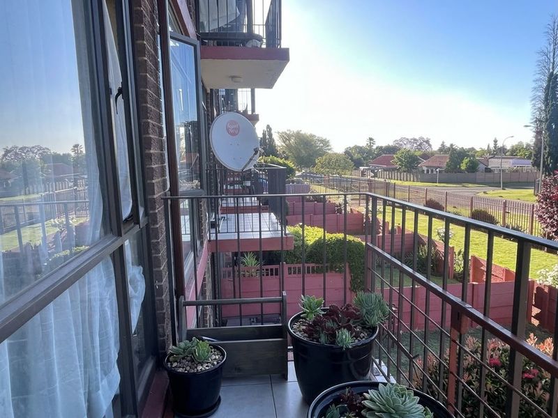 A functional apartment balcony featuring tiled flooring, a metal balustrade, and views over the surrounding residential complex and garden area.