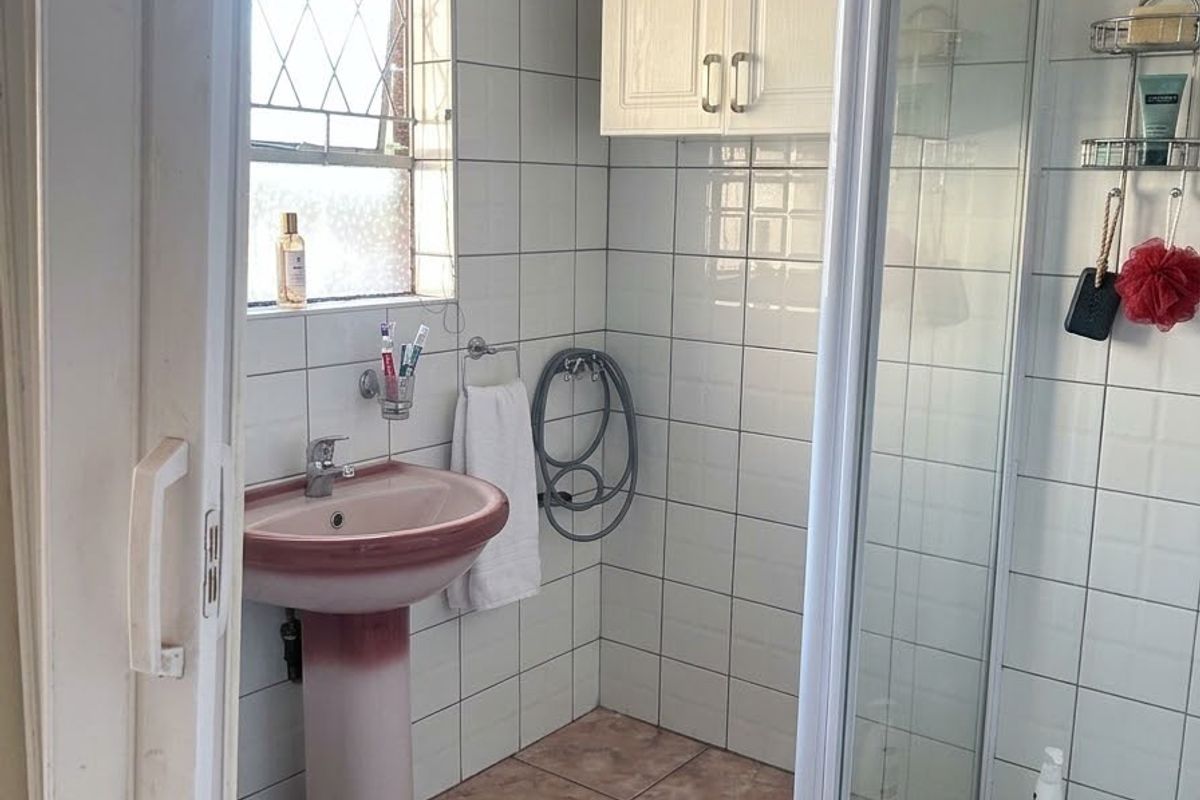 A functional bathroom featuring a pedestal basin, shower enclosure, and wall-mounted cabinetry, finished with tiled walls and flooring.