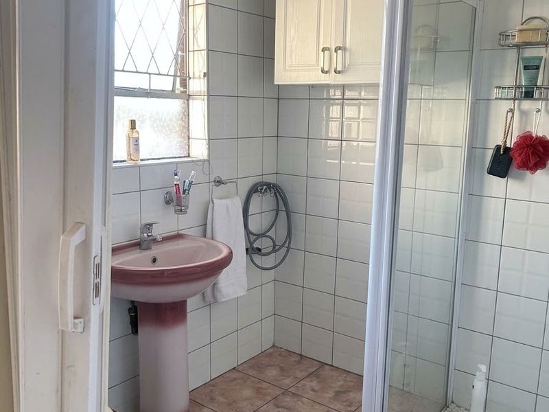 A functional bathroom featuring a pedestal basin, shower enclosure, and wall-mounted cabinetry, finished with tiled walls and flooring.