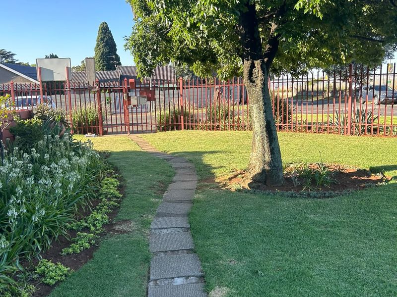 A well-maintained garden featuring a paved walkway, mature tree, and secure metal perimeter fencing.