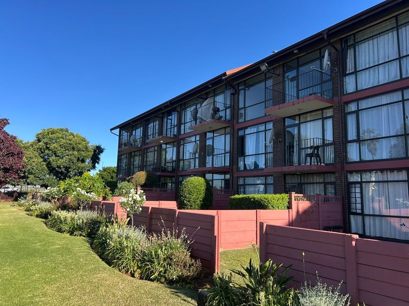 Rear view of a multi-story apartment building featuring brick facade, private balconies with metal railings, and a well-maintained communal garden area.