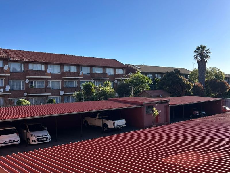 An elevated view of a residential apartment complex featuring covered parking bays with corrugated metal roofing and brick building exteriors.