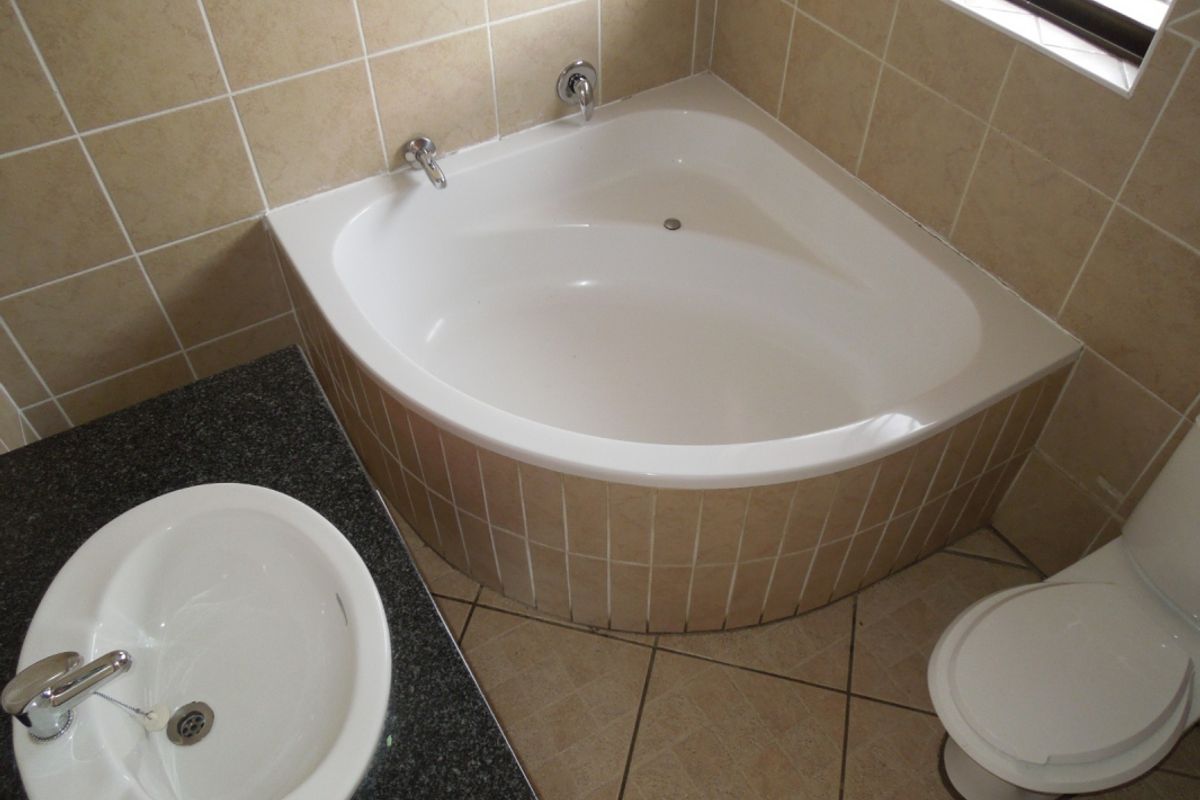 A functional bathroom featuring a corner bathtub, vanity basin with granite countertop, and neutral ceramic tiling throughout.