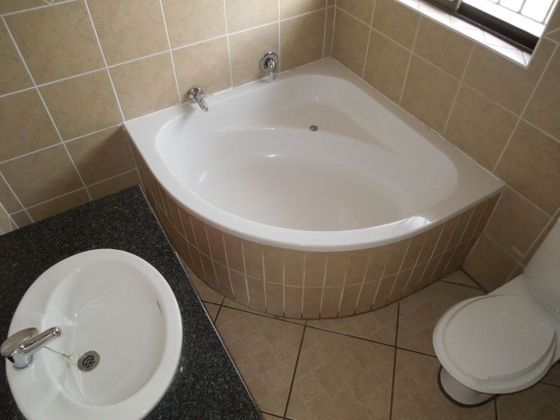 A functional bathroom featuring a corner bathtub, vanity basin with granite countertop, and neutral ceramic tiling throughout.