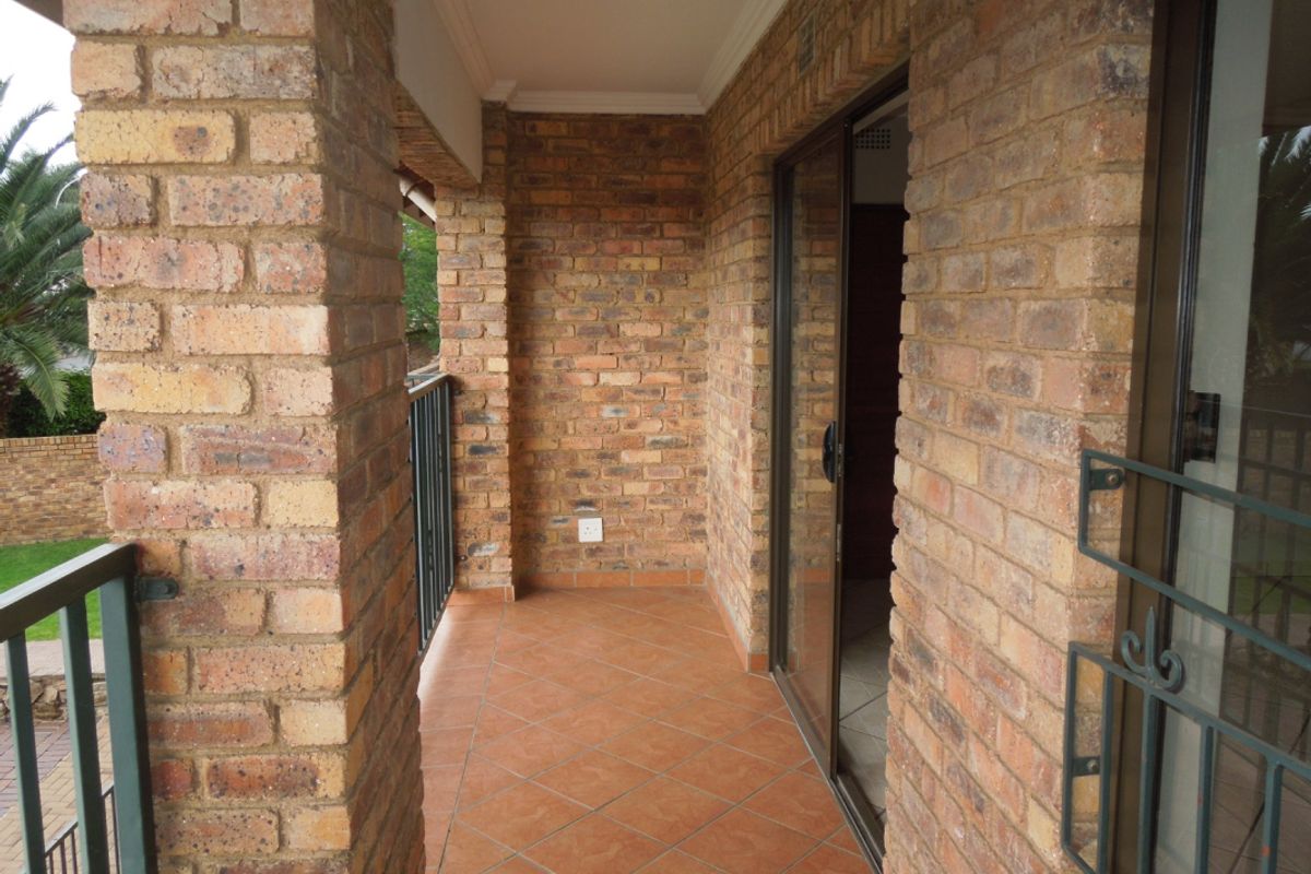 A covered balcony featuring exposed brick walls, tiled flooring, and a metal balustrade, providing a private outdoor space accessible via a sliding glass door.