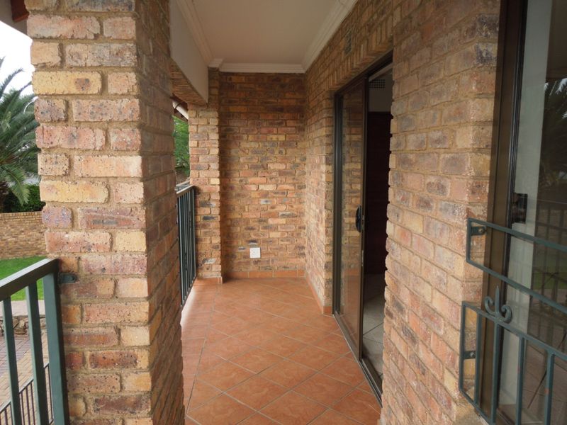 A covered balcony featuring exposed brick walls, tiled flooring, and a metal balustrade, providing a private outdoor space accessible via a sliding glass door.
