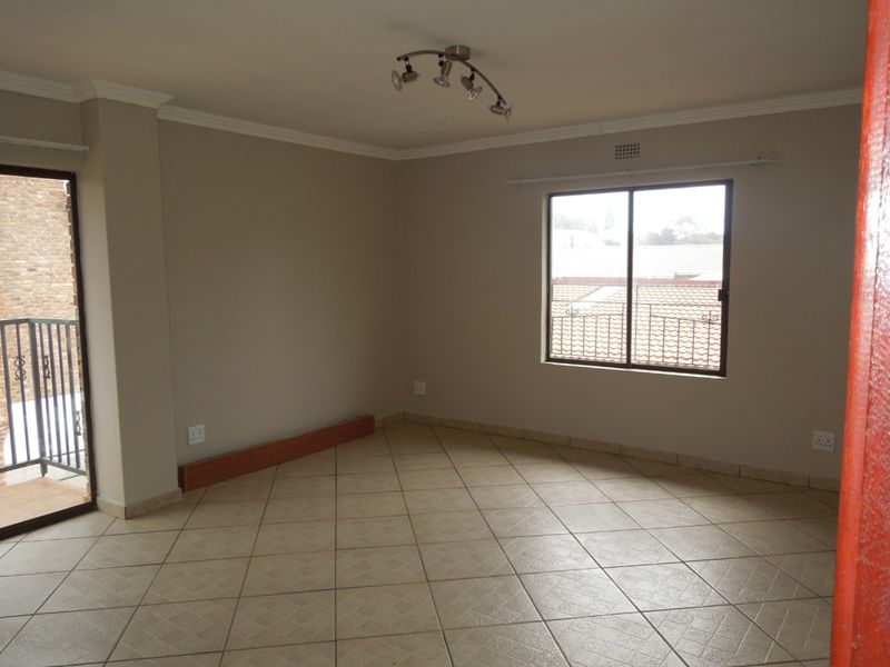 An empty living room featuring tiled flooring, neutral walls, a ceiling spotlight fixture, and access to a small balcony through a sliding glass door.