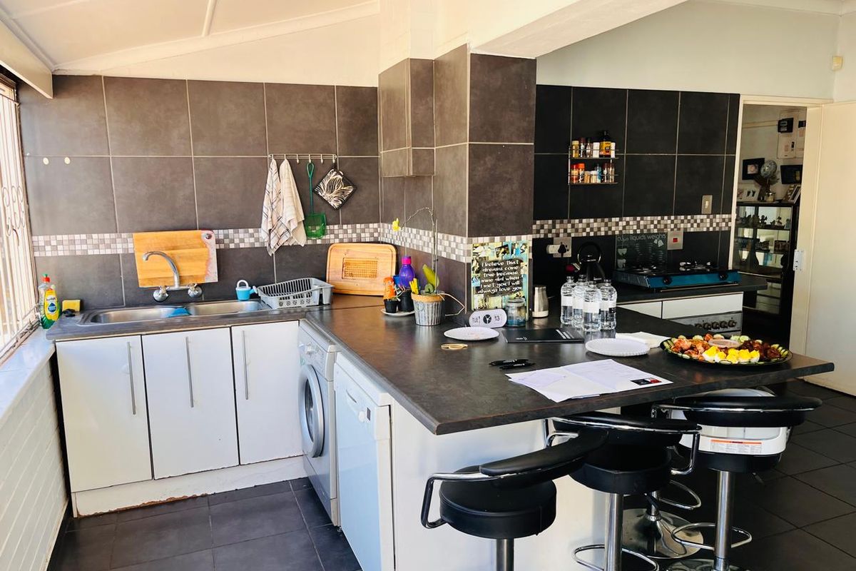 A functional kitchen featuring dark tiled walls, ample cabinetry, a double sink, and a breakfast bar area with integrated appliances.