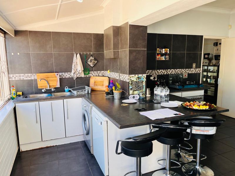 A functional kitchen featuring dark tiled walls, ample cabinetry, a double sink, and a breakfast bar area with integrated appliances.