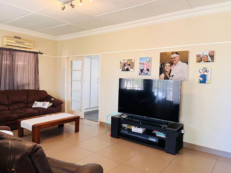 A comfortable living room featuring tiled flooring, coved ceilings, and an integrated air conditioning unit, with direct access to an adjacent room.