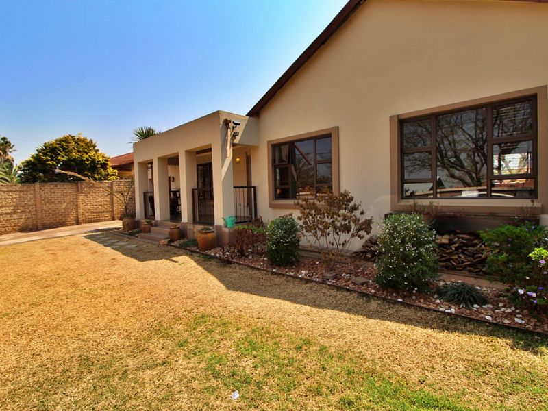 Rear view of the property featuring a covered patio, established garden beds, and a brick boundary wall.