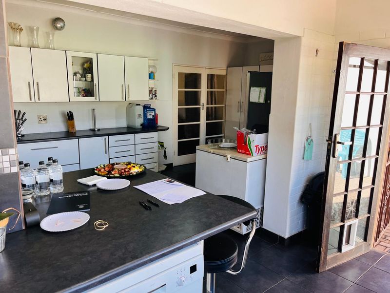 A functional kitchen featuring white cabinetry, dark laminate countertops, tiled flooring, and a glass-paneled french door leading to the exterior.