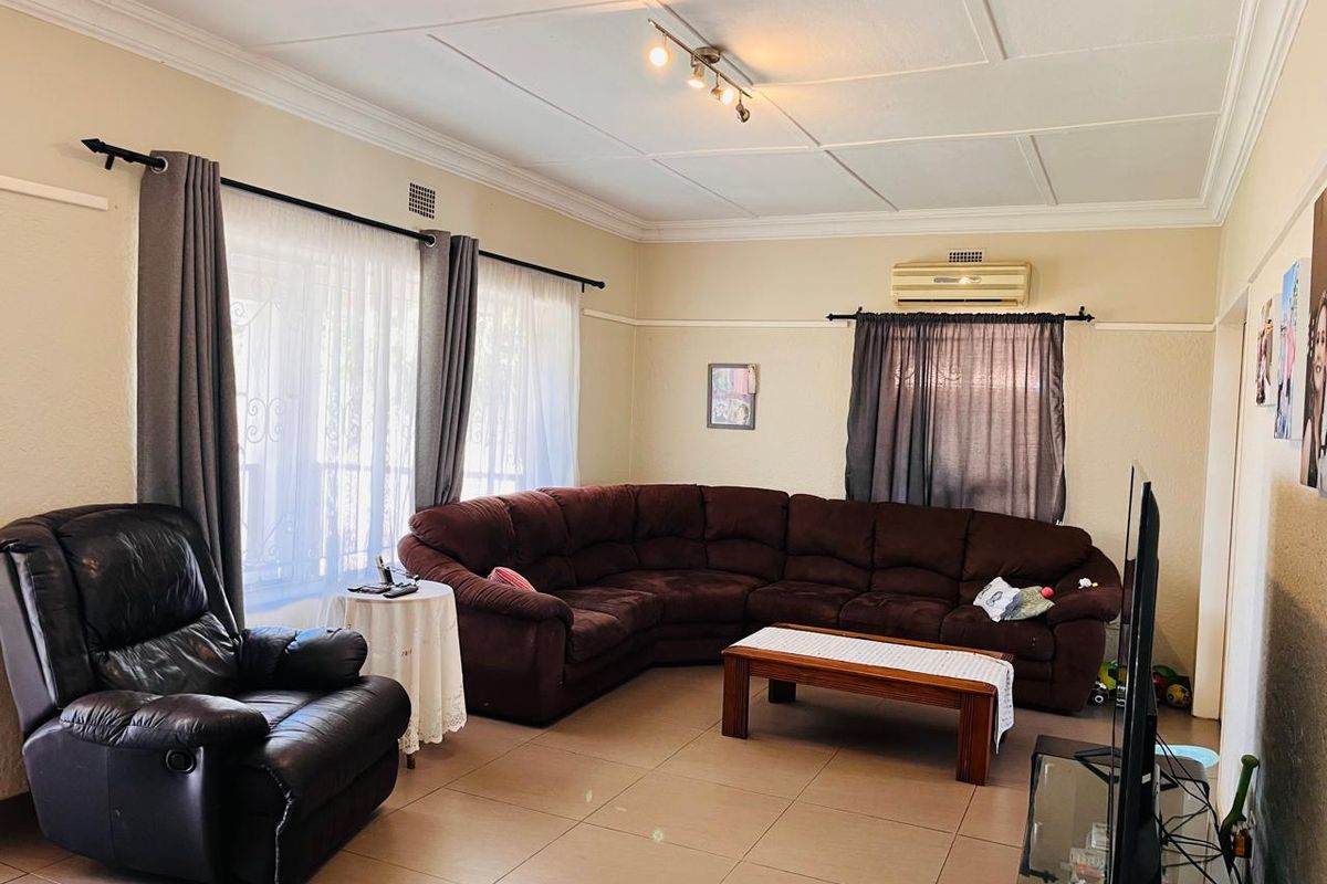 A spacious living room featuring tiled flooring, a coved ceiling, and a wall-mounted air conditioning unit, providing a comfortable and functional living space.