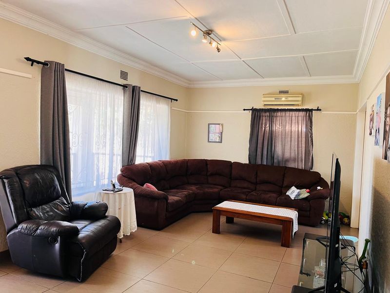 A spacious living room featuring tiled flooring, a coved ceiling, and a wall-mounted air conditioning unit, providing a comfortable and functional living space.