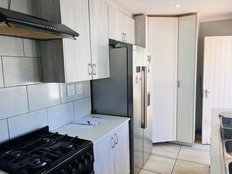 A functional kitchen featuring light wood-grain cabinetry, a gas stove with extractor fan, tiled backsplash, and a convenient built-in pantry cupboard.