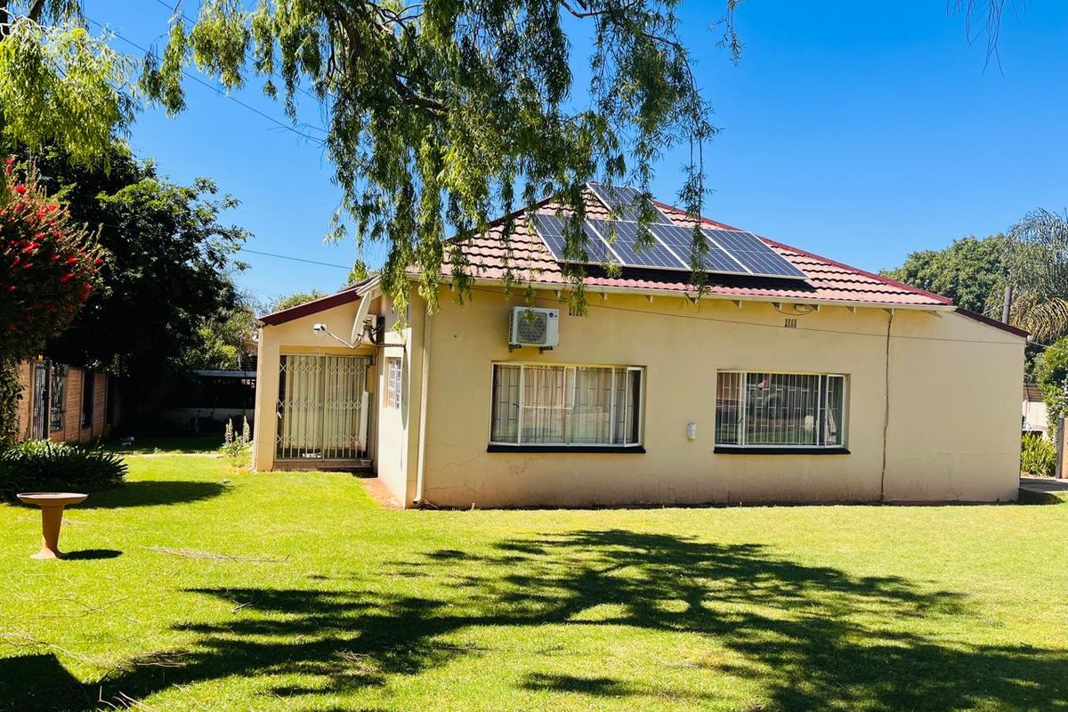 Rear view of the house featuring a tiled roof with solar panels, an exterior air conditioning unit, and a spacious garden.