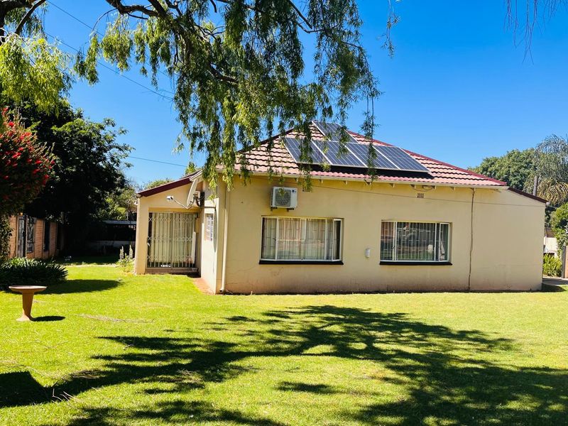 Rear view of the house featuring a tiled roof with solar panels, an exterior air conditioning unit, and a spacious garden.