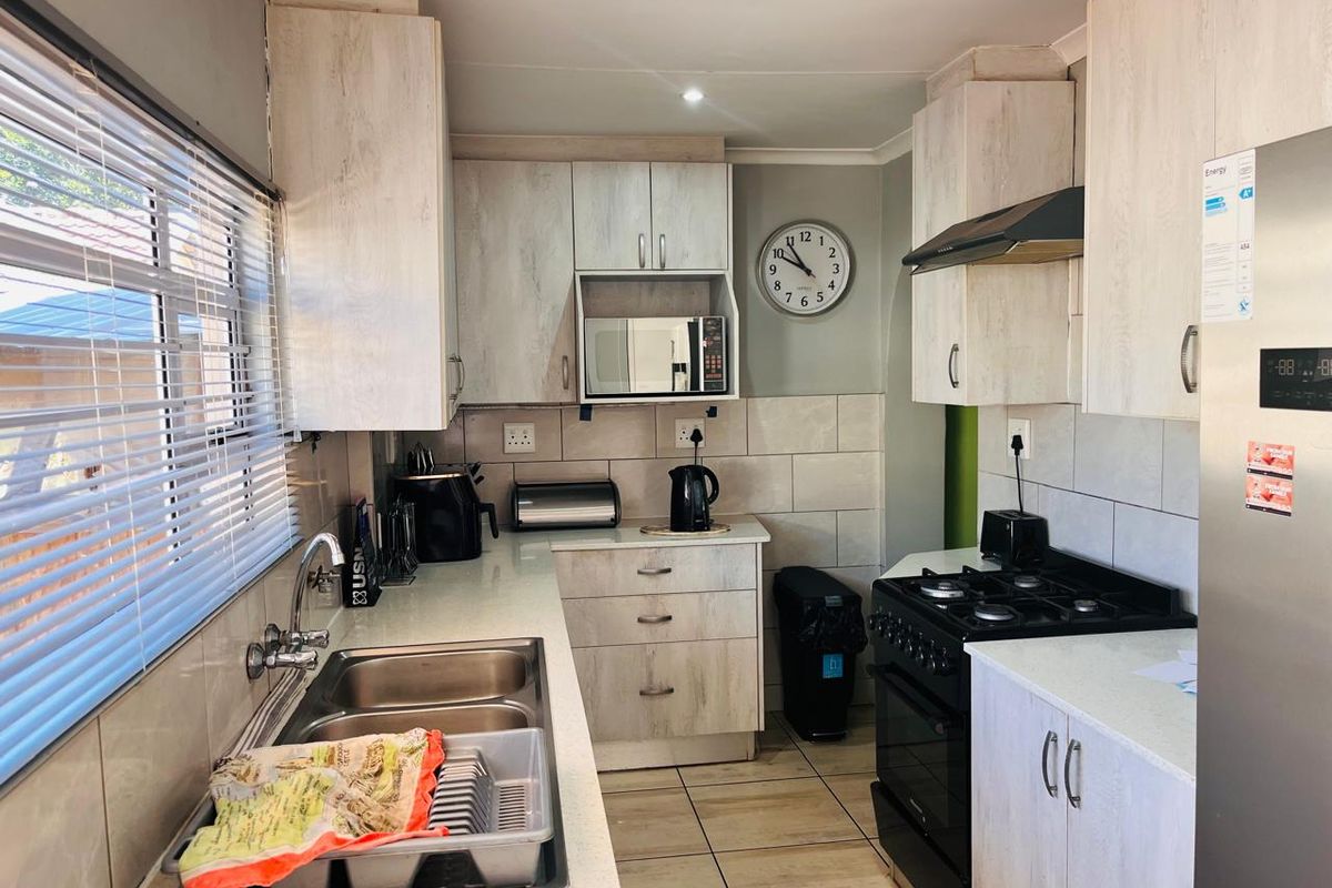 A functional kitchen featuring light-toned built-in cabinetry, a double basin sink, tiled backsplash, and integrated appliance housing.