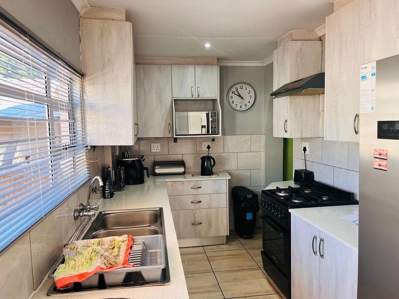A functional kitchen featuring light-toned built-in cabinetry, a double basin sink, tiled backsplash, and integrated appliance housing.