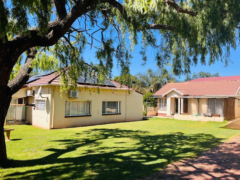 Rear view of the property featuring a spacious lawn, tiled roof structures, solar panels, and security bars on windows.