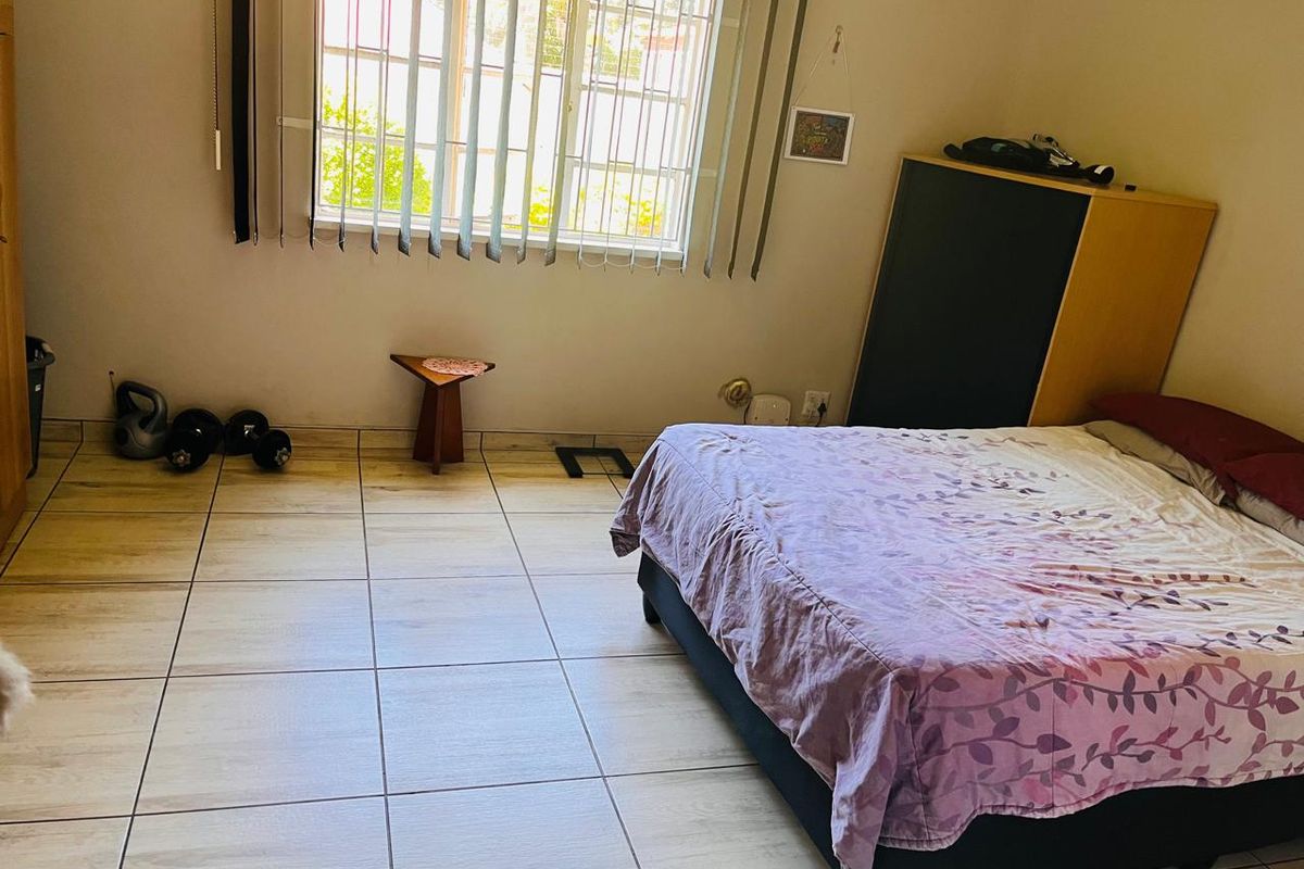A bedroom featuring tiled flooring and vertical blinds, providing a functional space with natural light.