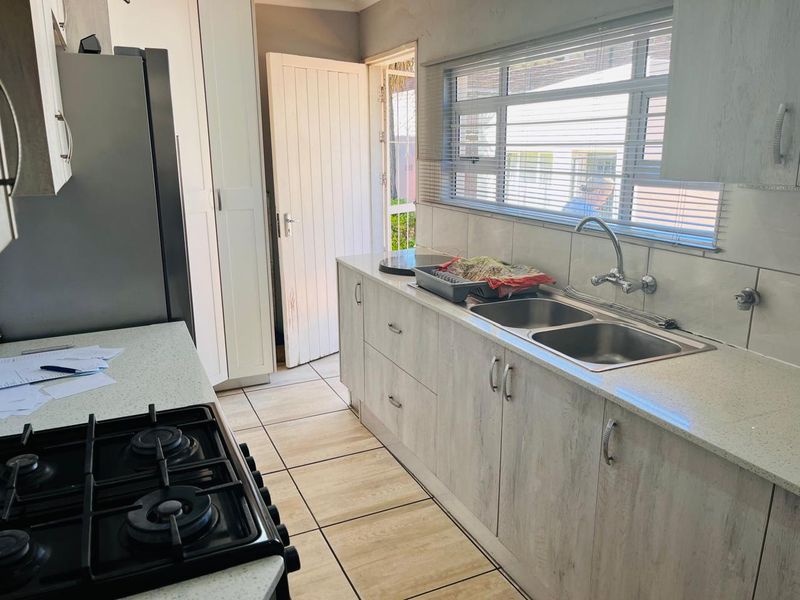 A functional kitchen featuring light-toned cabinetry, a double stainless steel sink, gas hob, and tiled flooring with direct access to the exterior.
