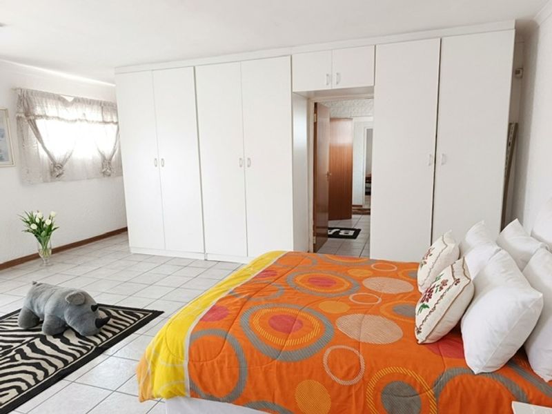 Spacious bedroom featuring extensive white built-in cupboards and neutral tiled flooring, offering ample storage and a clean, functional layout.