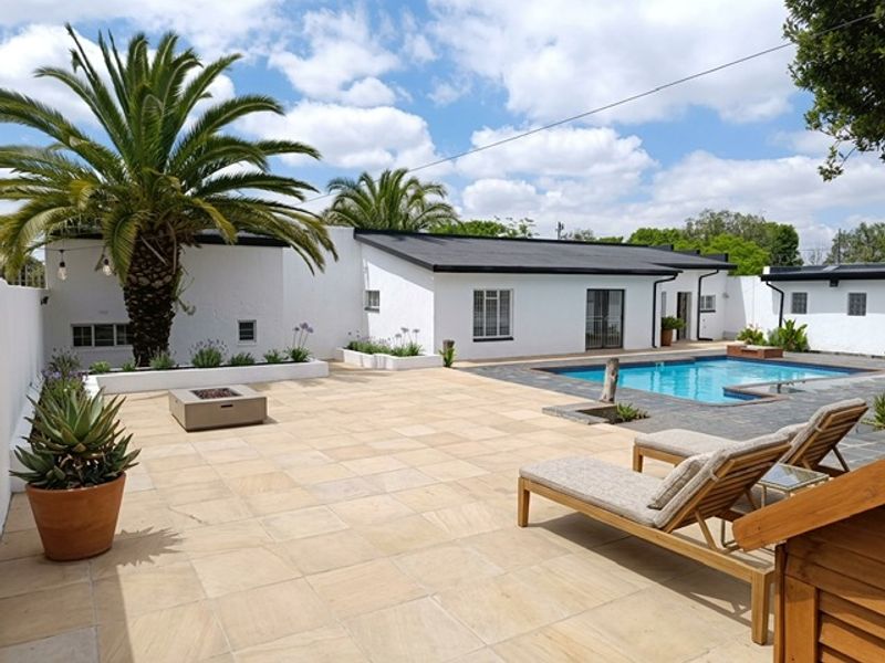 Spacious outdoor entertainment area featuring a swimming pool, paved patio, built-in fire pit, and raised garden beds against a white rendered exterior.