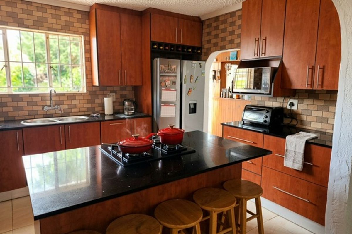 A functional kitchen featuring wooden cabinetry, granite countertops, a central island with a gas hob, and a tiled backsplash.