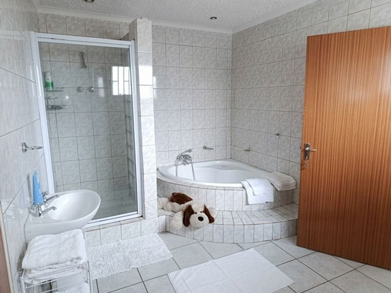 A functional bathroom featuring a corner bathtub, a separate tiled shower enclosure, and a wall-mounted basin with neutral ceramic tiling throughout.