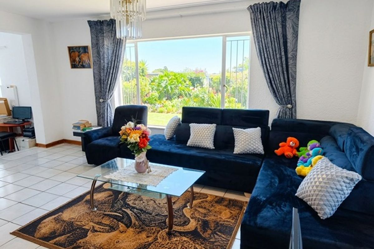 Spacious living room featuring large picture windows with garden views, ceramic tiled flooring, and a decorative crystal chandelier.