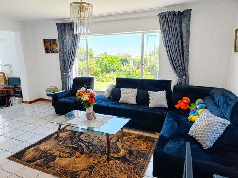 Spacious living room featuring large picture windows with garden views, ceramic tiled flooring, and a decorative crystal chandelier.