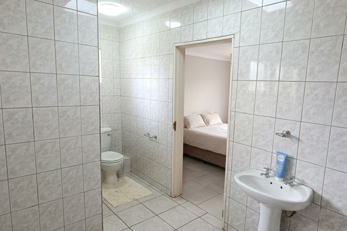A functional bathroom featuring a pedestal basin and toilet, finished with neutral ceramic wall and floor tiles.
