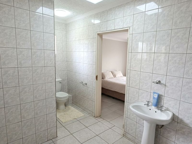 A functional bathroom featuring a pedestal basin and toilet, finished with neutral ceramic wall and floor tiles.