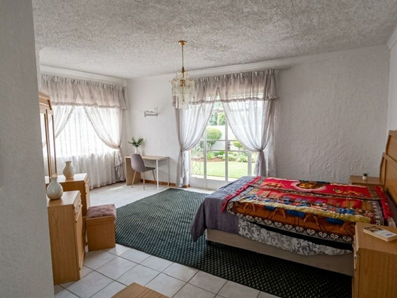 Spacious bedroom featuring tiled flooring, a textured ceiling, and direct access to the garden through a glass sliding door.