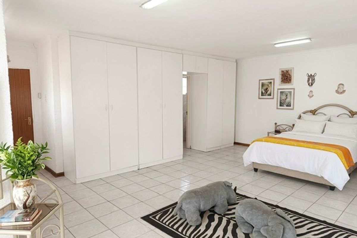 Spacious bedroom featuring extensive built-in cupboards, neutral tiled flooring, and bright overhead lighting, offering a functional and well-maintained living space.