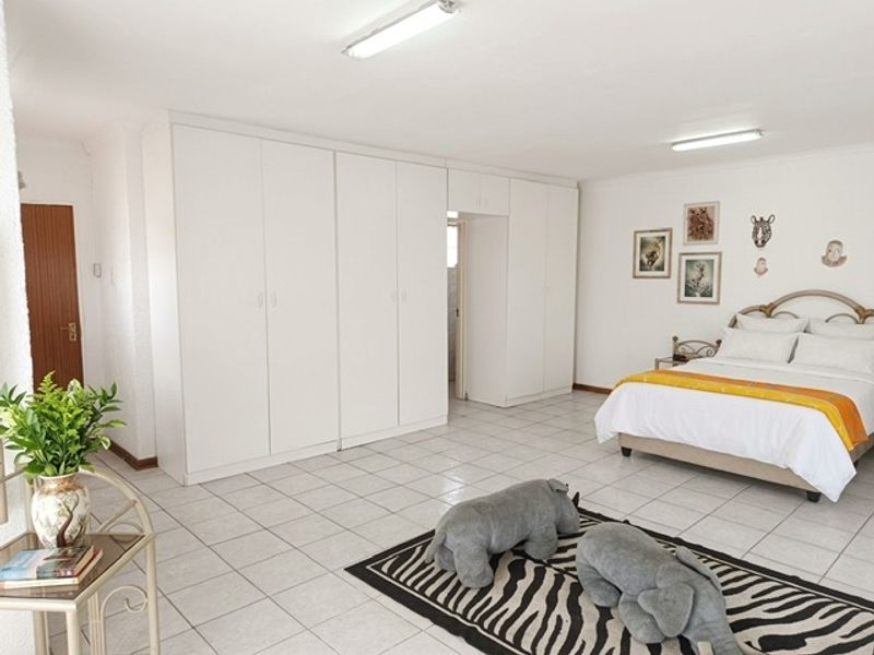 Spacious bedroom featuring extensive built-in cupboards, neutral tiled flooring, and bright overhead lighting, offering a functional and well-maintained living space.